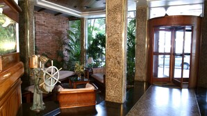 A lobby with a ship's wheel, a brick wall, and a reception desk. - Hotel Villa do Mar (Balneário Camboriú)