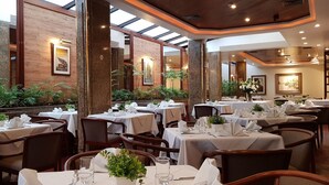 A restaurant with multiple tables set for dining, featuring a mix of natural and artificial lighting, wooden and stone decor, and indoor plants. - Hotel Villa do Mar (Balneário Camboriú)