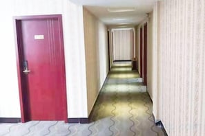 Un pasillo de hotel con una puerta roja, alfombra estampada y un largo corredor con puertas al final.