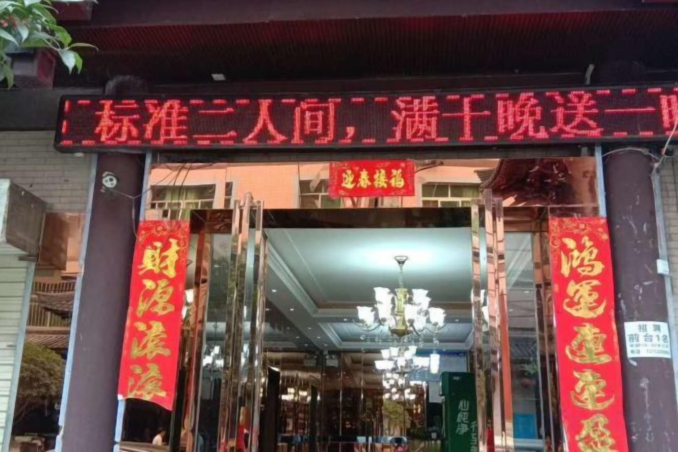 A hotel entrance with a traditional Chinese architectural style, featuring a red neon sign above the entrance and two red banners on either side.