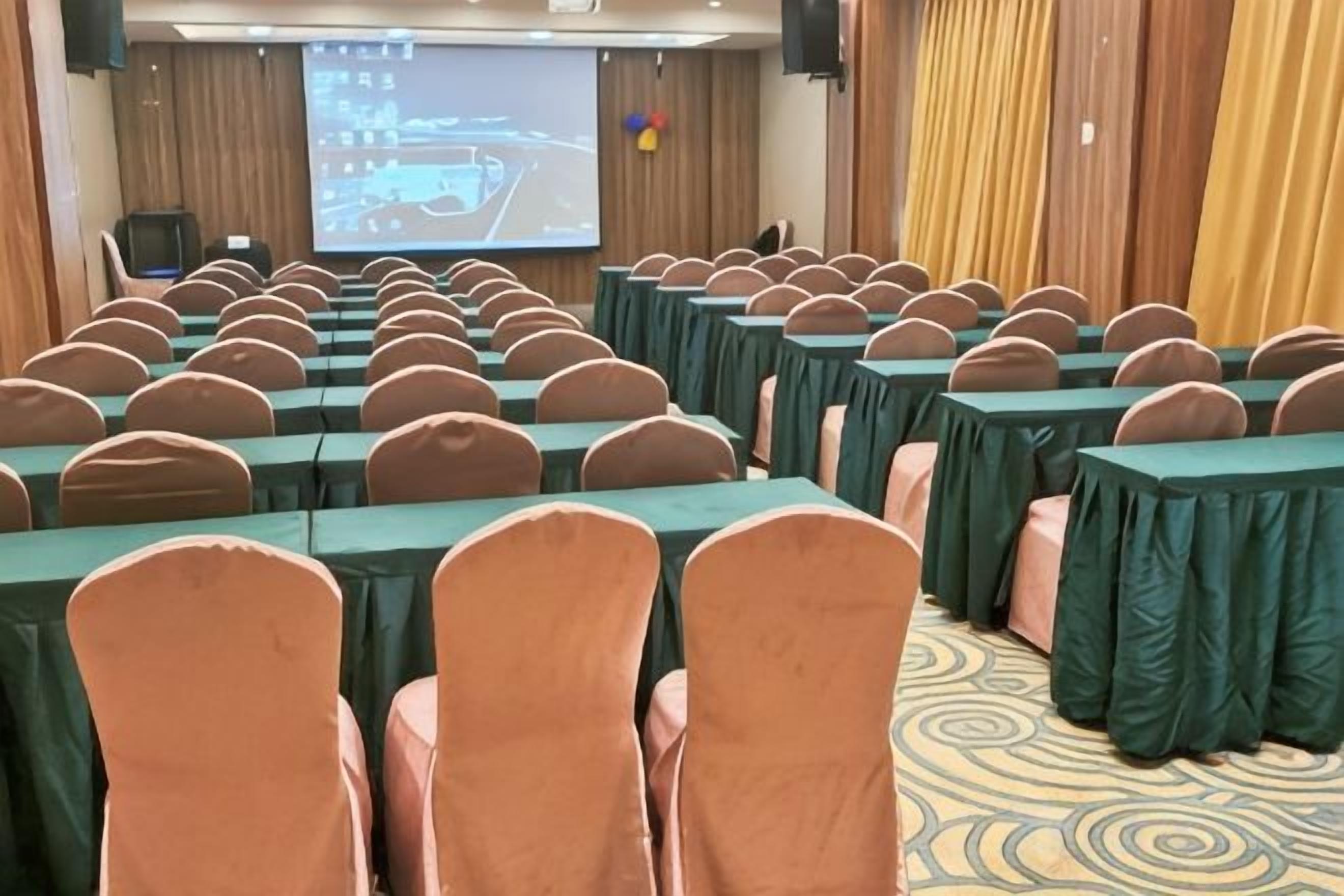 A conference room with rows of tables and chairs, a projection screen, and a carpeted floor.