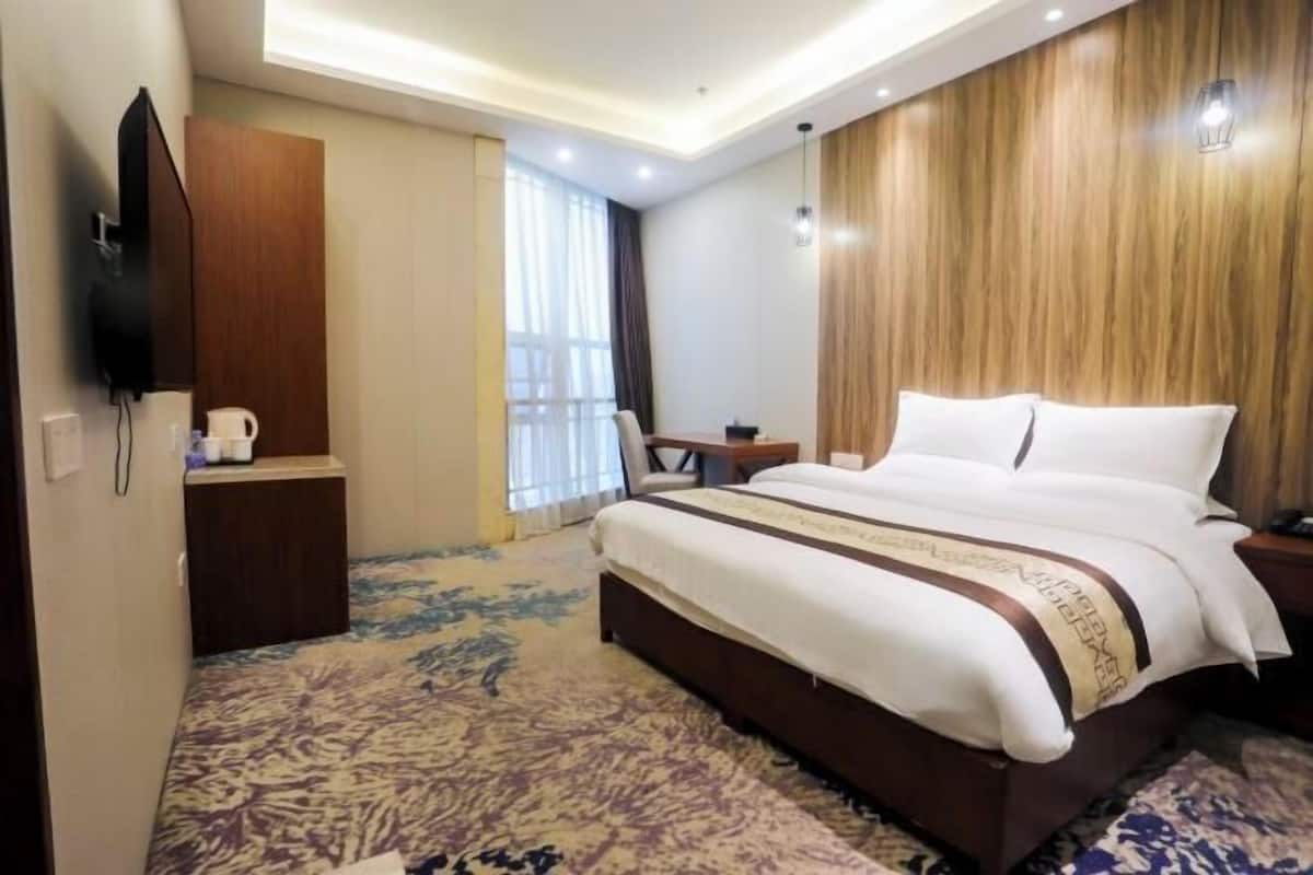 Ein Hotelzimmer mit einem großen Bett, einem Schreibtisch, einem Stuhl, einem Fernseher und einem Fenster mit Vorhängen.