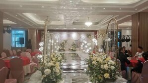 A banquet hall with tables set for a formal event, decorated with floral arrangements and a central aisle. - Xinji Holiday Hotel (Nanchang)