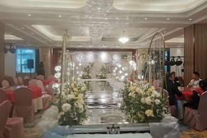 A banquet hall with tables set for a formal event, decorated with floral arrangements and a central aisle. - Xinji Holiday Hotel (Nanchang)