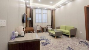 A hotel room with a sofa, a coffee table, a TV, a desk with a lamp, and a window with curtains. - Xinji Holiday Hotel (Nanchang)