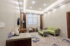 A hotel room with a sofa, a coffee table, a TV, a desk with a lamp, and a window with curtains. - Xinji Holiday Hotel (Nanchang)