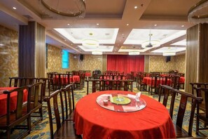 Une salle de banquet avec des tables rondes, des nappes rouges et des chaises en bois.