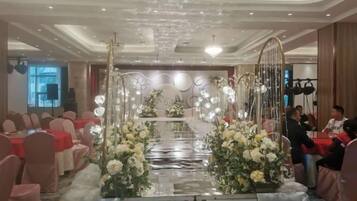 A banquet hall with a central aisle, tables on either side, and a decorative archway with floral arrangements.