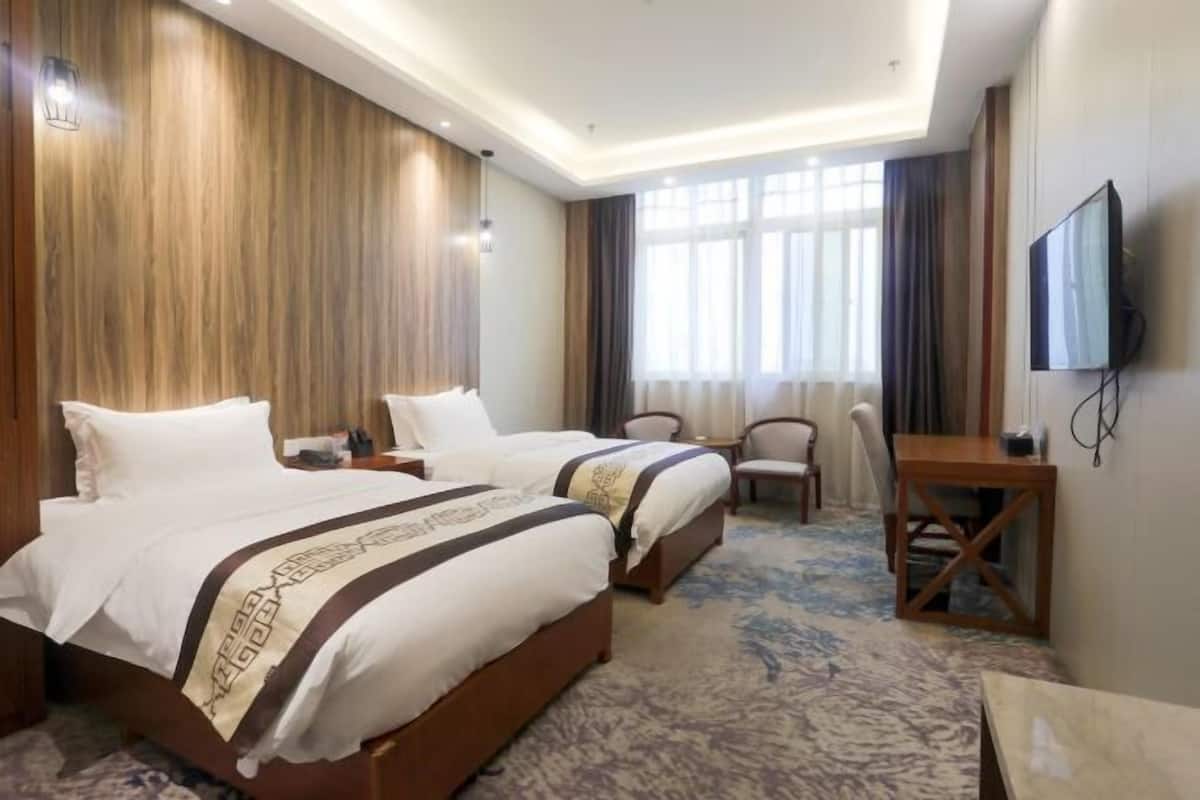 Ein Hotelzimmer mit zwei Betten, einem Fernseher, einem Schreibtisch und einem großen Fenster.