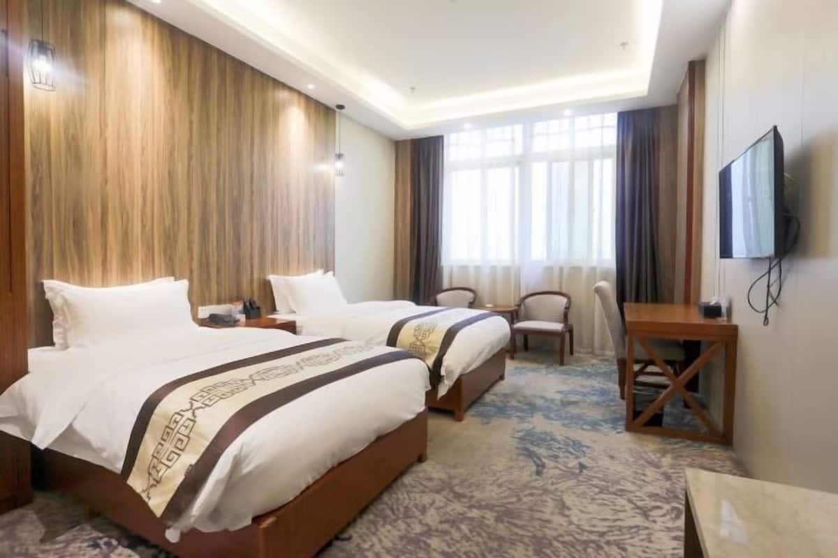 Ein Hotelzimmer mit zwei Betten, einem Schreibtisch, einem Fernseher und einem großen Fenster.