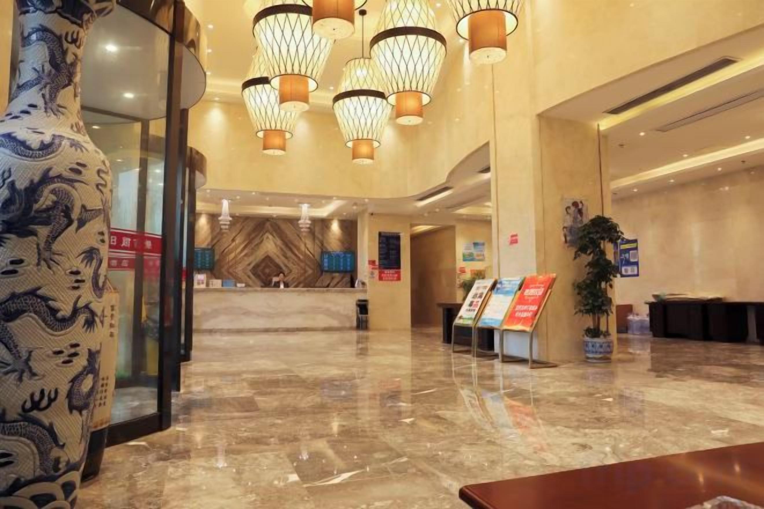 A hotel lobby with a reception desk, a large decorative vase, and a modern chandelier.