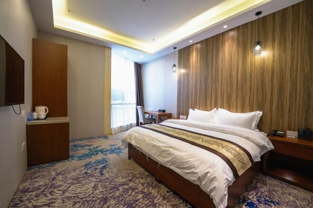 Quarto de hotel com uma cama grande, uma mesa, uma cadeira, uma TV de tela plana e uma janela com cortinas.