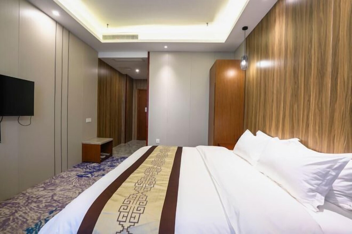 Quarto de hotel com uma cama grande, televisão de tela plana na parede e painel de parede de madeira.