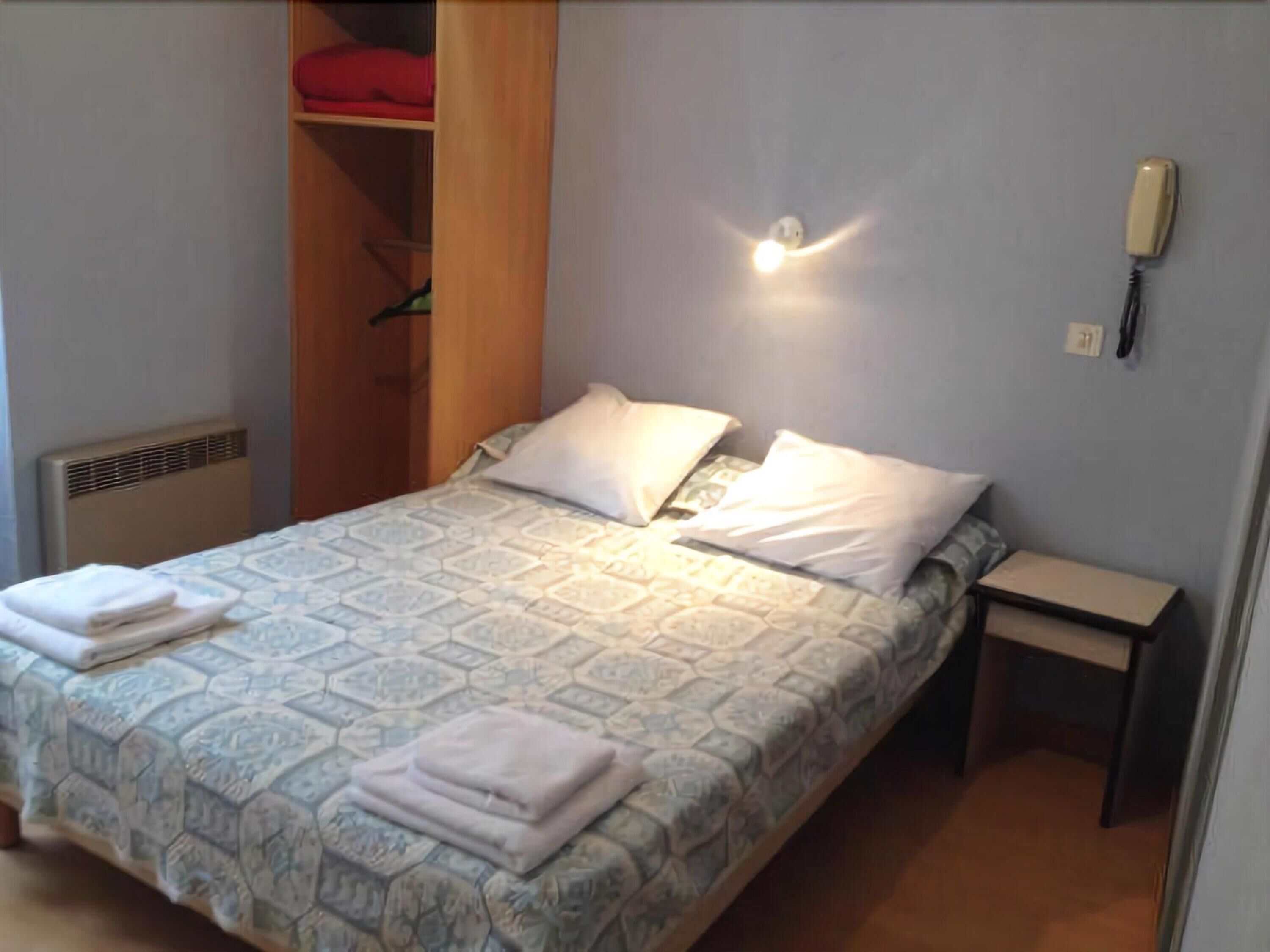 A neatly made bed with a patterned bedspread, a bedside table with a phone, and a closet with a red item visible.