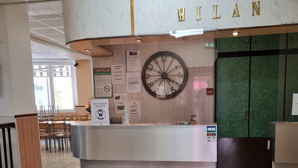 Zona de recepción de hotel con una pared de mármol, un reloj y una puerta verde.