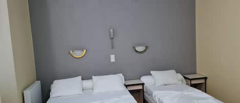 A hotel room with two single beds, a bedside table, a wall-mounted telephone, and a radiator.