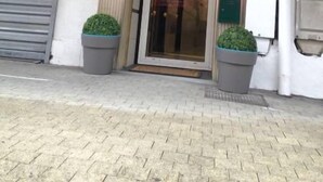 Entrada de un hotel con un letrero rojo que dice "HOTEL LE MILAN 39" y un cartel de bienvenida sobre la puerta.