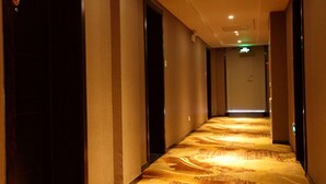 A hotel corridor with a patterned carpet, dark walls, and doors leading to rooms.
