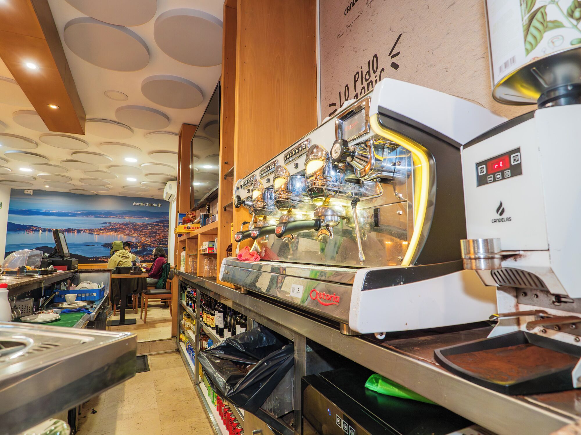 Un bar de café con un mural de paisaje urbano, una barra de madera y una máquina de café.