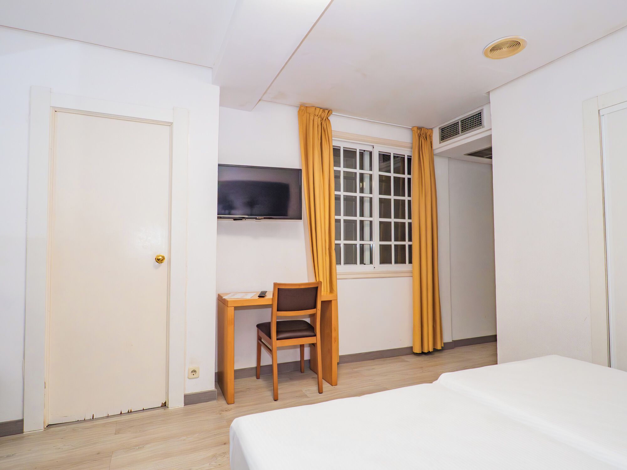 A hotel room with a bed, a desk with a chair, a television, and a window with curtains.