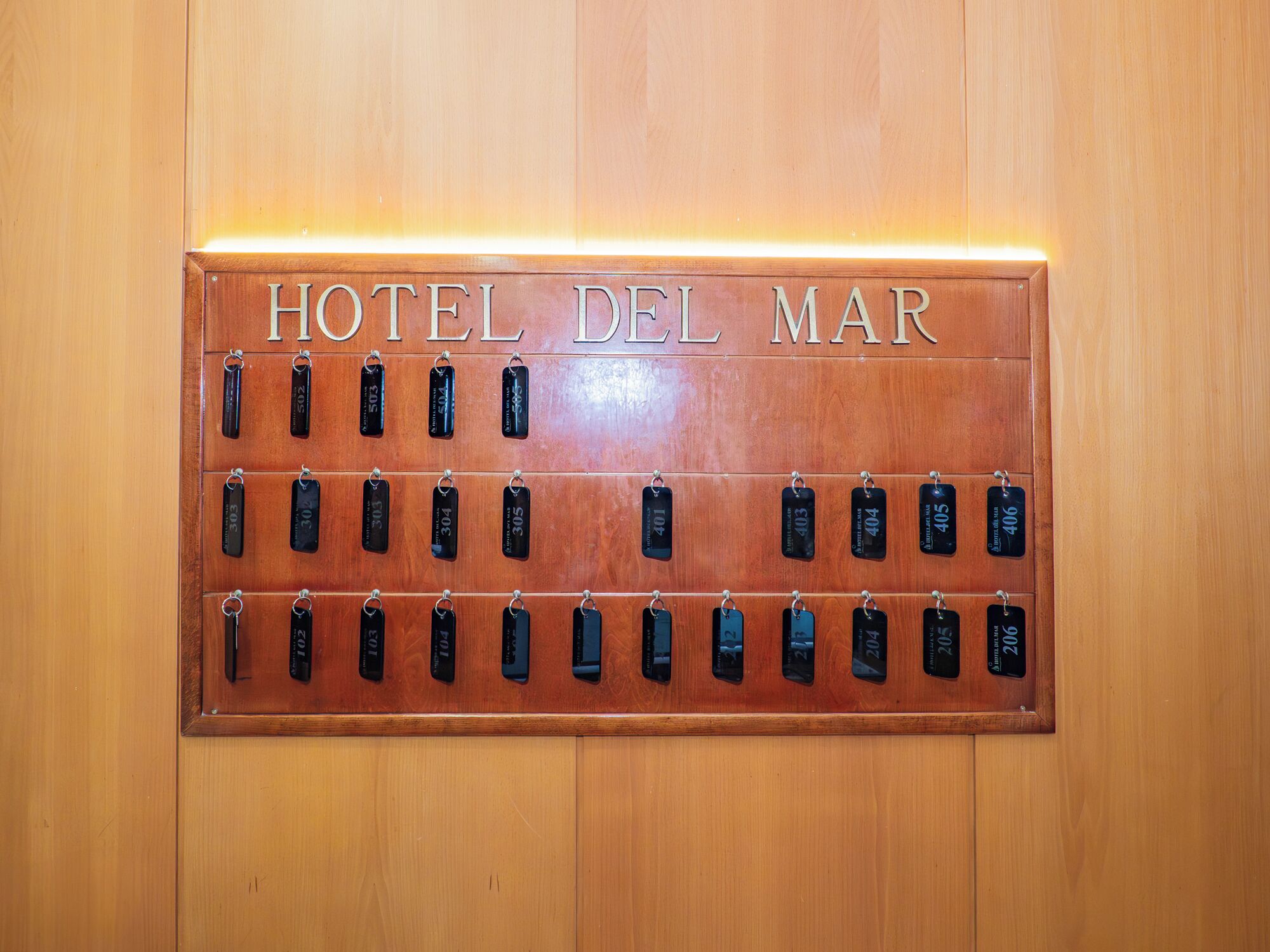 A wooden wall with a sign reading 'HOTEL DEL MAR' and a row of numbered keycards.