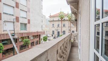 Un balcón con barandilla de piedra, con vista a una calle con edificios y coches estacionados.