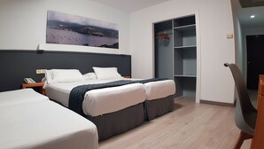 A hotel room with a bed, a bedside table with a phone, a wardrobe, and a painting on the wall. - Hotel del Mar (Vigo)
