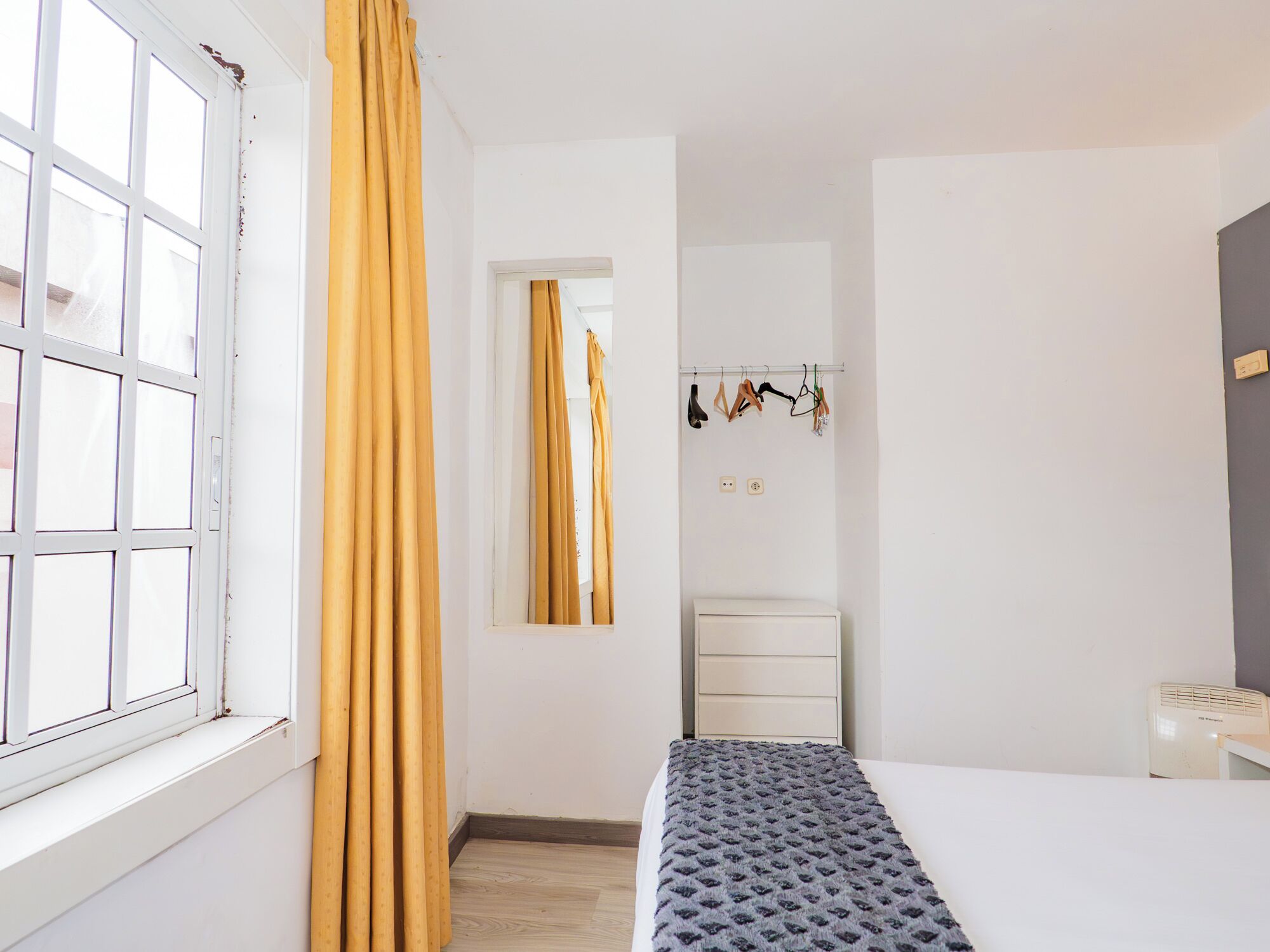 A room with a bed, a window with curtains, a wardrobe, and a radiator.