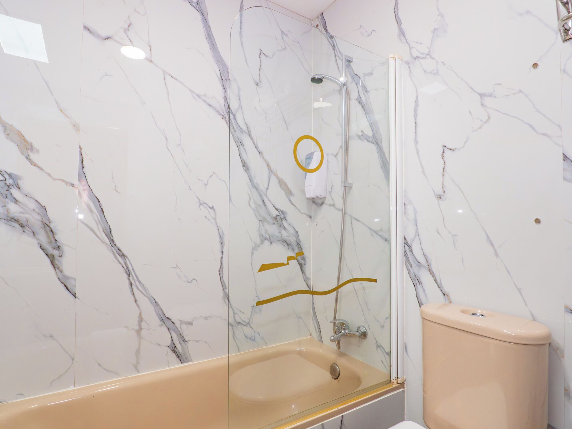 A bathroom with a marble wall, a glass shower enclosure, a beige bathtub, and a toilet.