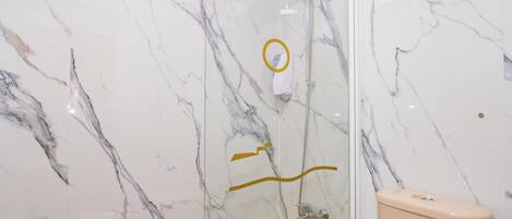 A bathroom with a marble wall, a glass shower enclosure, a beige bathtub, and a toilet.