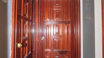 Una puerta de madera con una placa de número, un pasillo con números en la pared y un suelo con baldosas de color claro.
