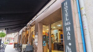 A hotel entrance with a sign reading 'HOTEL DEL MAR,' outdoor seating with chairs and tables, and a covered patio area. - Hotel del Mar (Vigo)