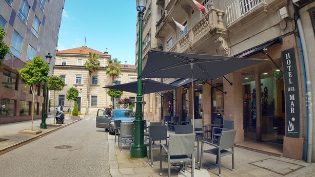 An outdoor seating area with umbrellas, a building with a sign reading "HOTEL DEL MAR", and a parked car. - Hotel del Mar (Vigo)