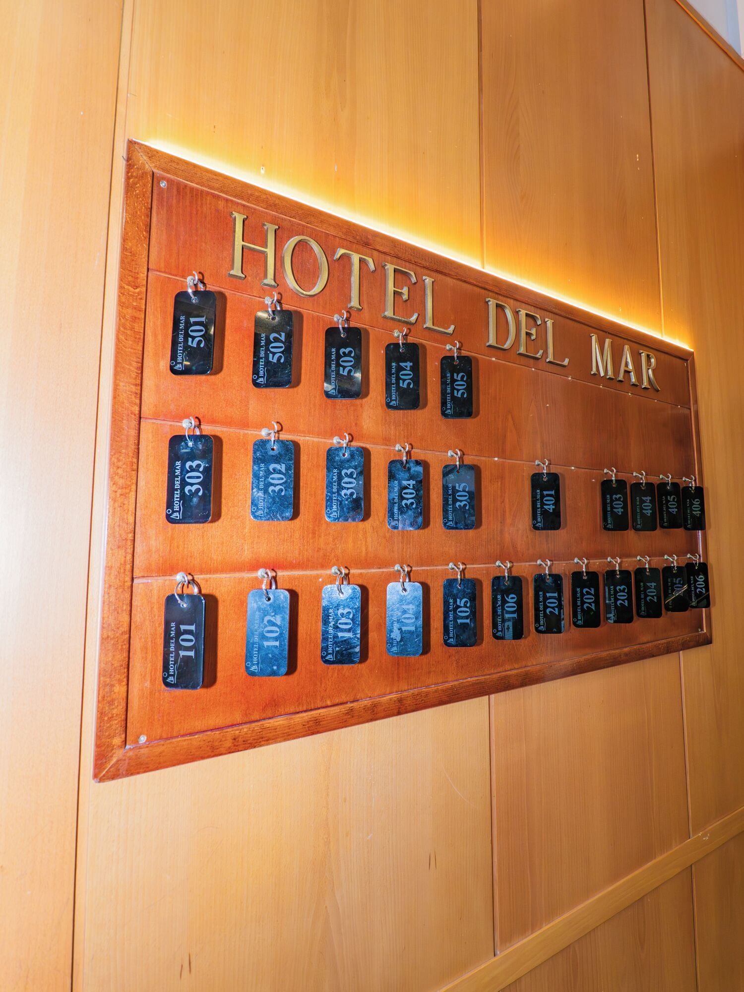 Un mur en bois sur lequel est affiché un panneau indiquant « HÔTEL DEL MAR » et une série de plaques numérotées indiquant les numéros de chambre.