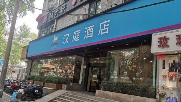 A hotel entrance with a blue sign, steps leading up to the door, and a parked scooter outside.