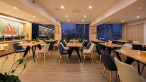 A modern dining area with tables and chairs, large windows with a city view, and a wall with abstract art.