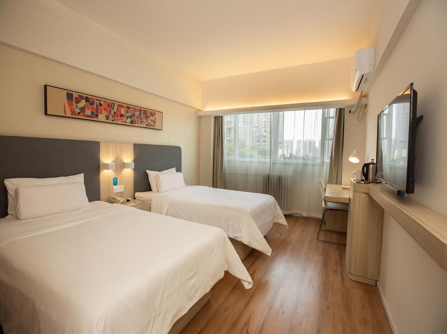 A hotel room with two beds, a desk, a television, and a window with a city view.