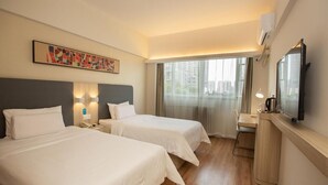 A hotel room with two beds, a desk, a television, and a window with a city view.
