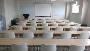 A classroom with rows of desks and chairs, a projector screen, and a whiteboard.