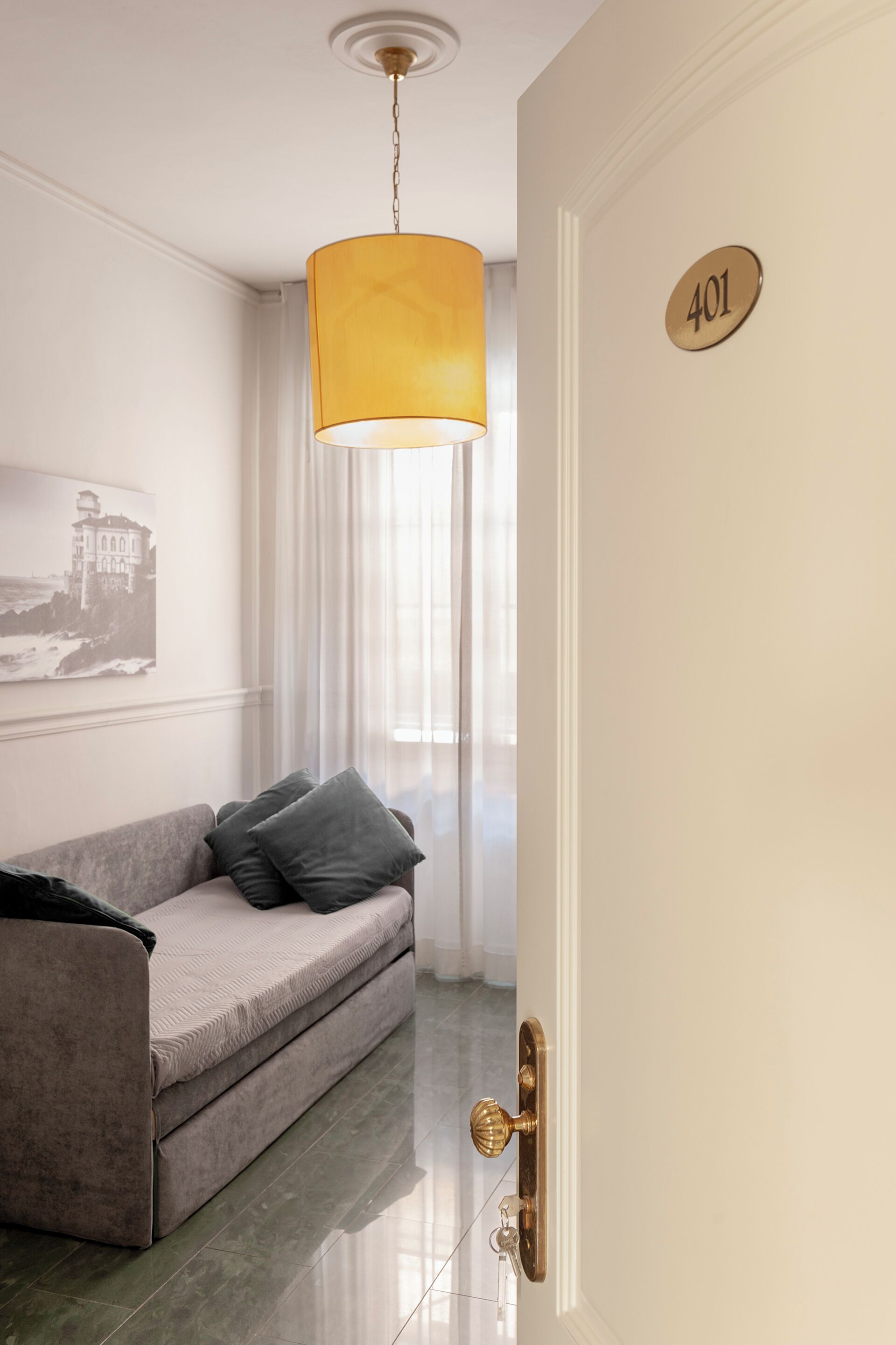A room with a sofa, a door with a number plate, and a hanging lamp.