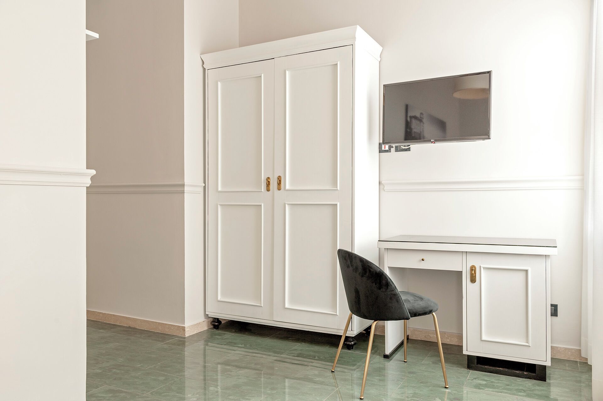 A room with a white wardrobe, a desk, and a black chair.