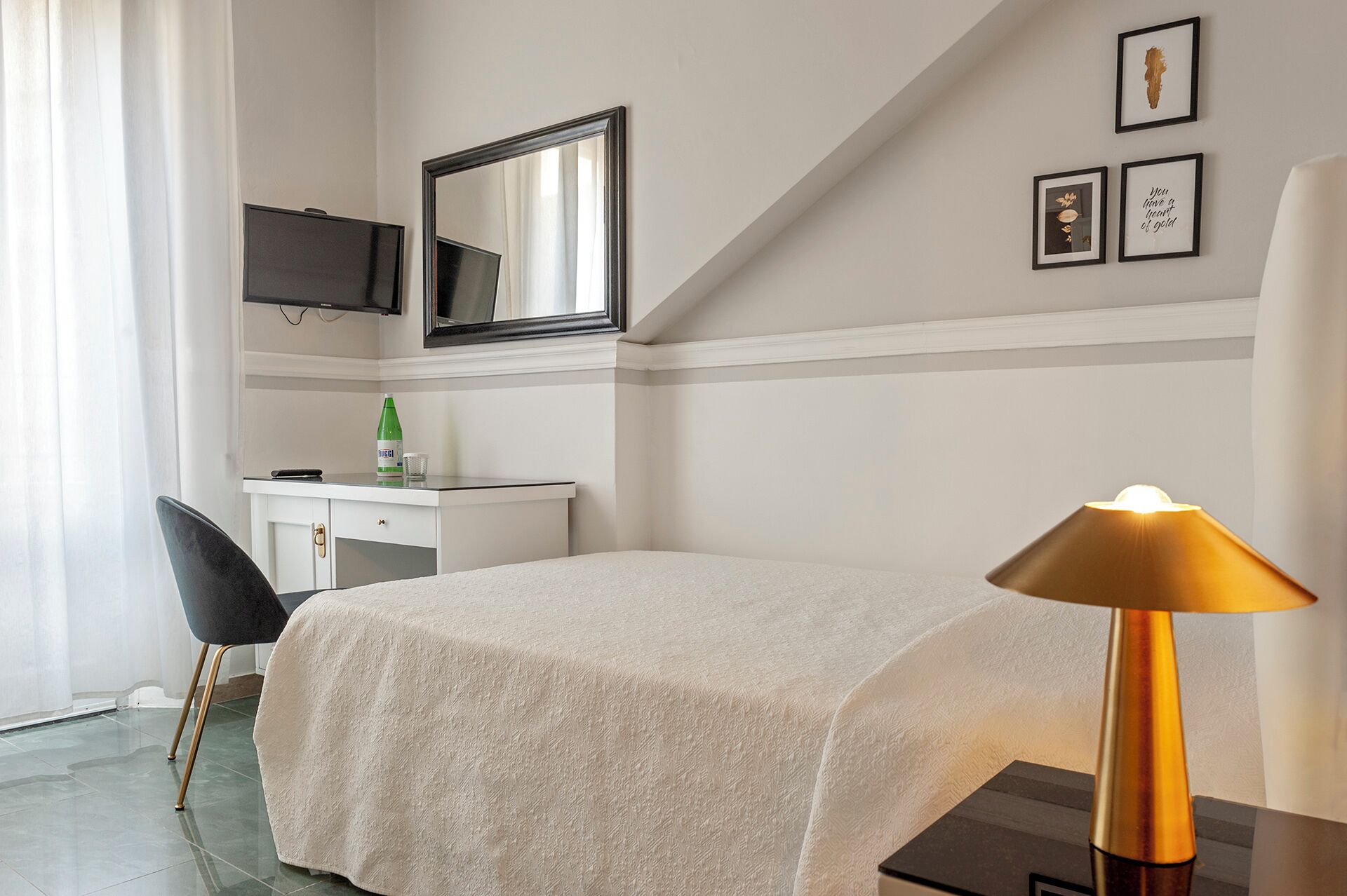Una habitación de hotel con una cama, un escritorio con una silla, un televisor y cuadros en la pared.