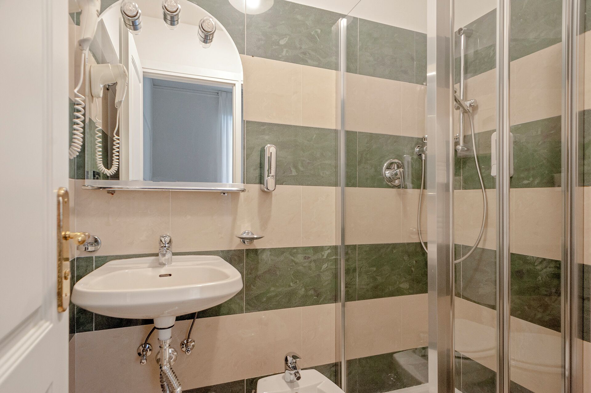 Une salle de bain avec un lavabo blanc, un miroir, un sèche-cheveux et une douche séparée par une paroi en verre.
