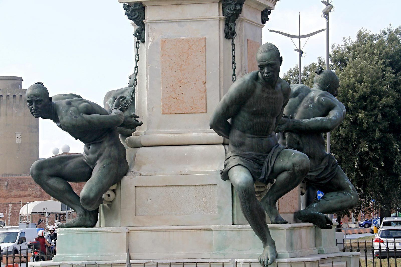 A bronze statue of three muscular figures in dynamic poses, mounted on a pedestal with a classical architectural design.