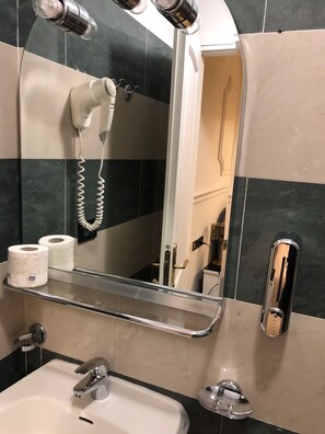 Een badkamer met een wastafel, spiegel, haardroger en handdoekhouder.
