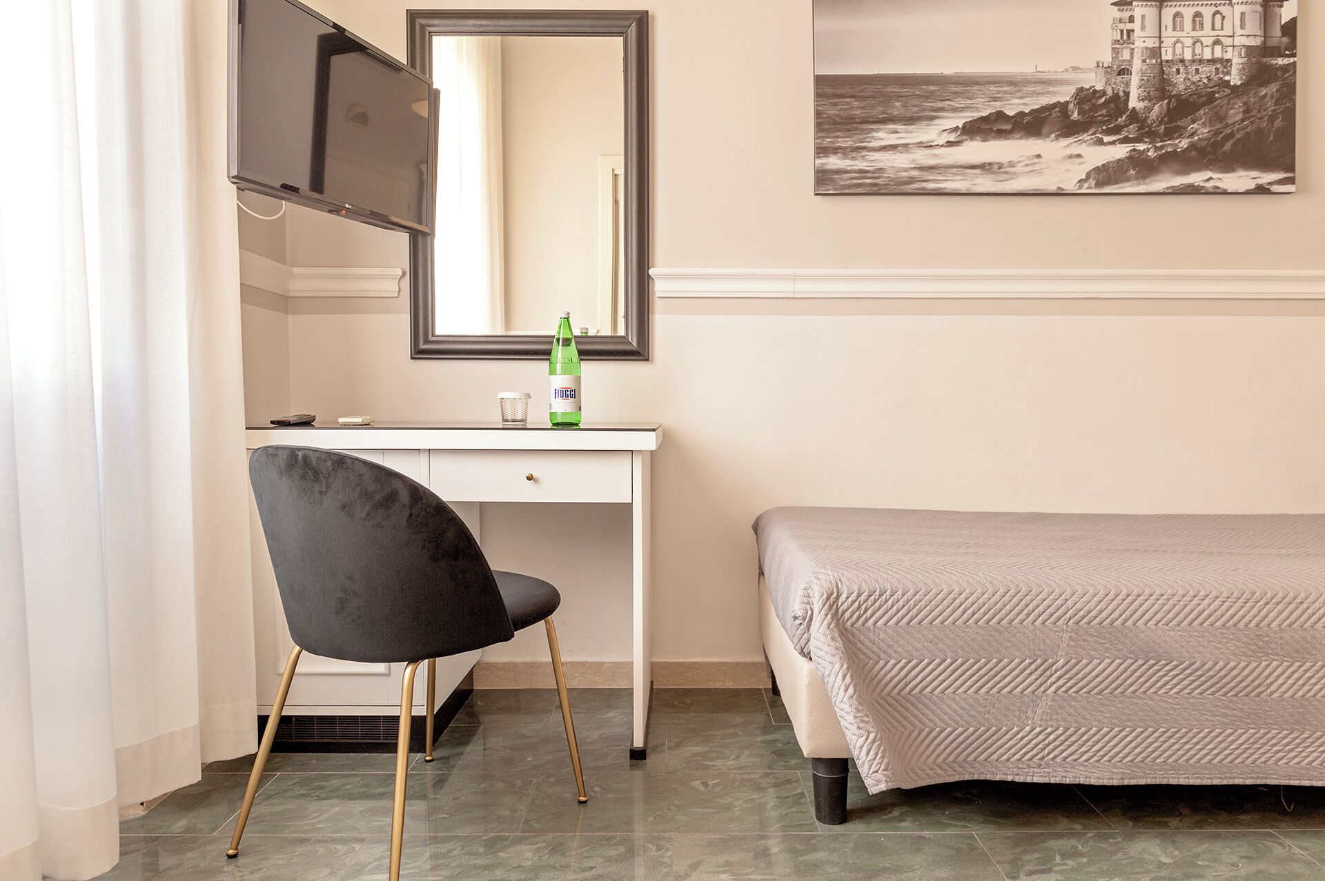 A bedroom with a bed, a desk with a chair, a mirror, and a bottle of water.