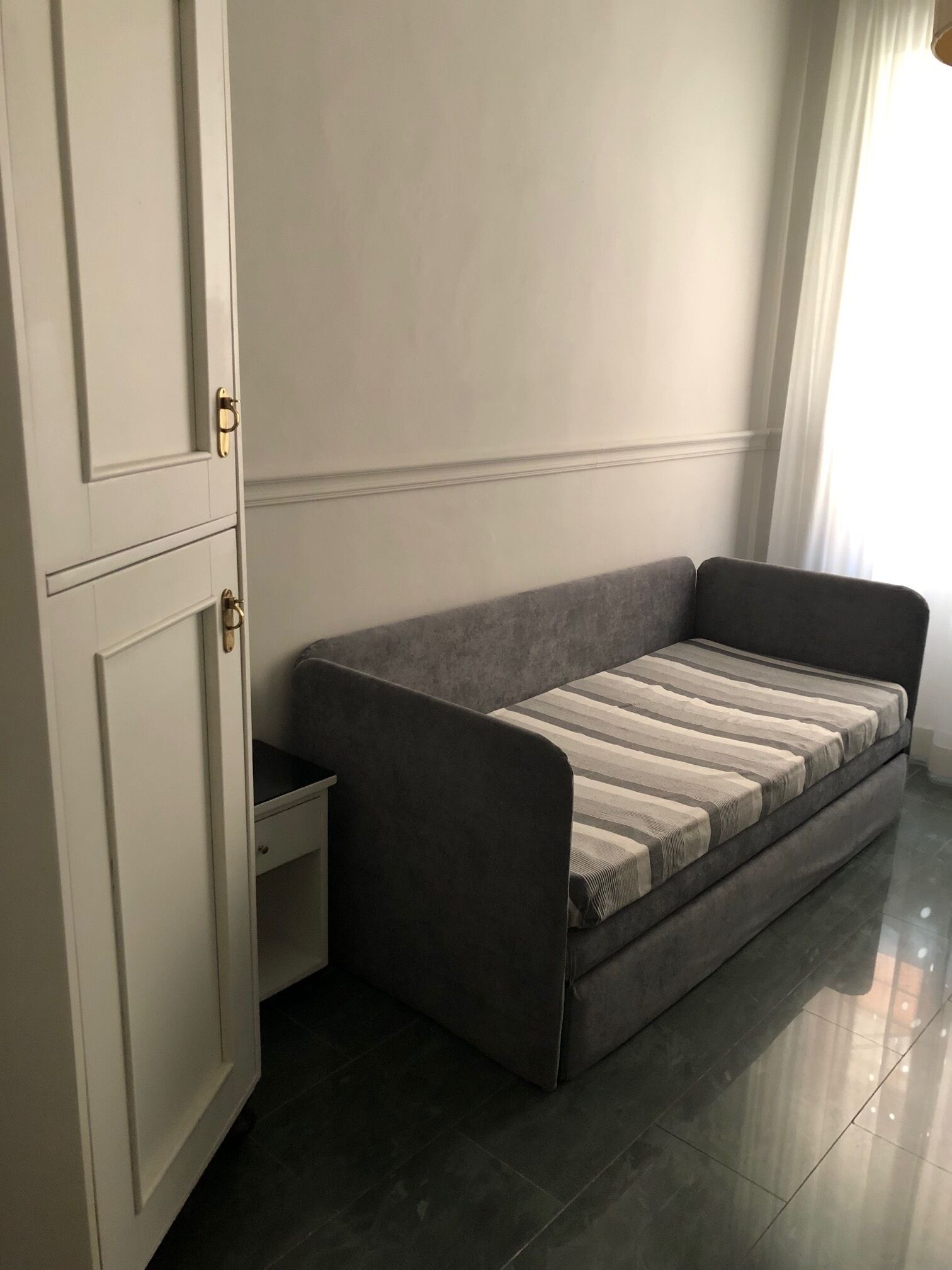 A modern room with a grey sofa, a white wardrobe, and a window with curtains.