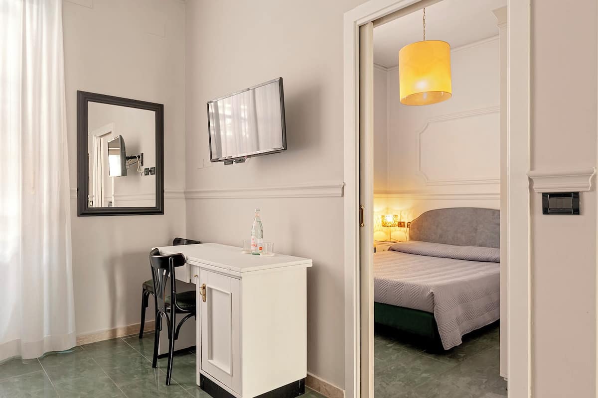 Une chambre d’hôtel comprenant un lit, un bureau avec une chaise, un téléviseur fixé au mur et une porte donnant sur une autre pièce.