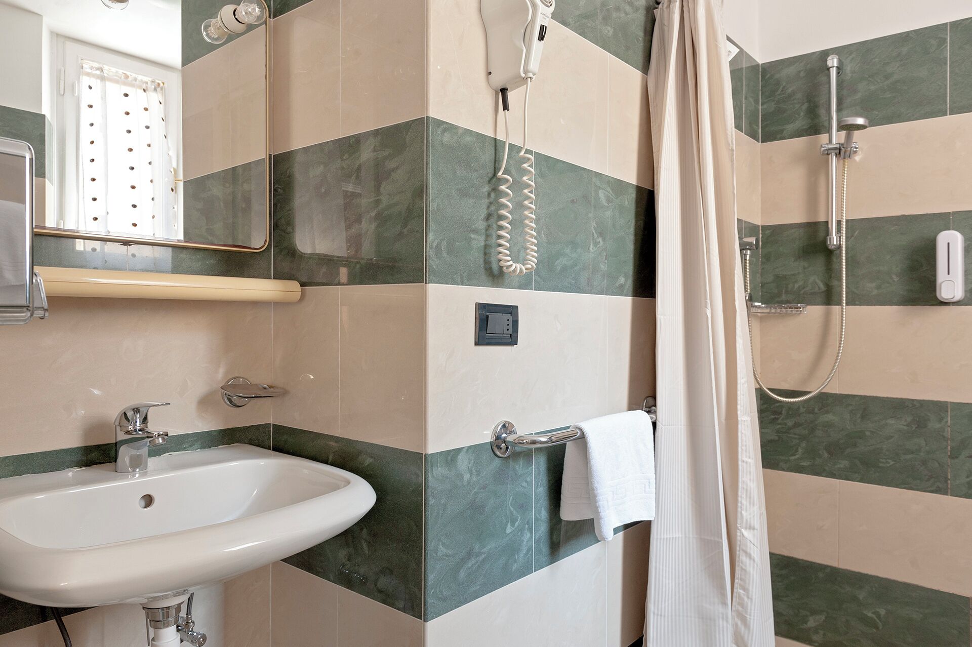 A bathroom with a sink, mirror, shower, and towel rack.