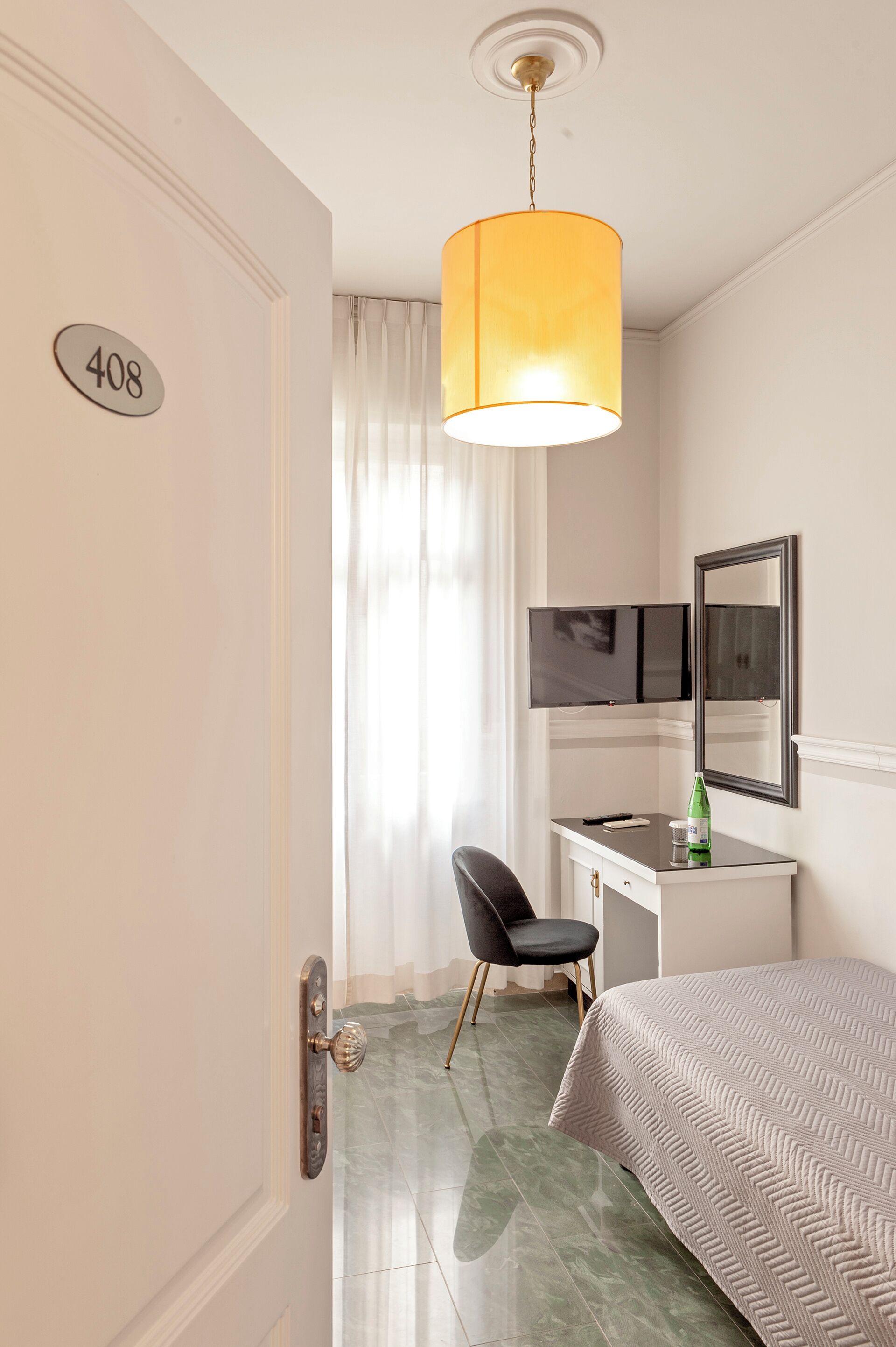 A hotel room with a bed, a desk, a chair, a television, and a mirror.